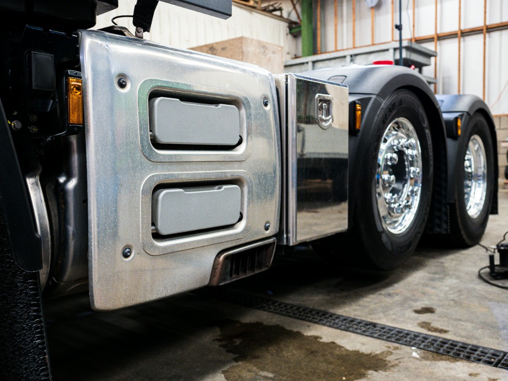 Heavy truck in the workshop showing custom fabricated metal panels, chassis detail, and alloy wheels